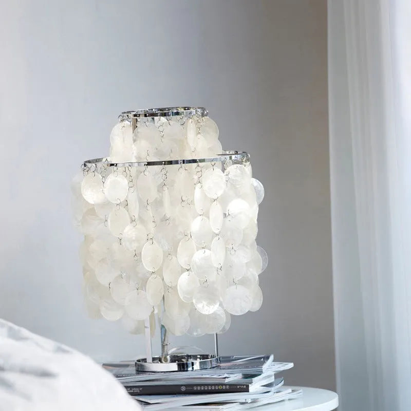 Modern shell-shaped metal bedside table lamp in chrome finish on a wooden table.