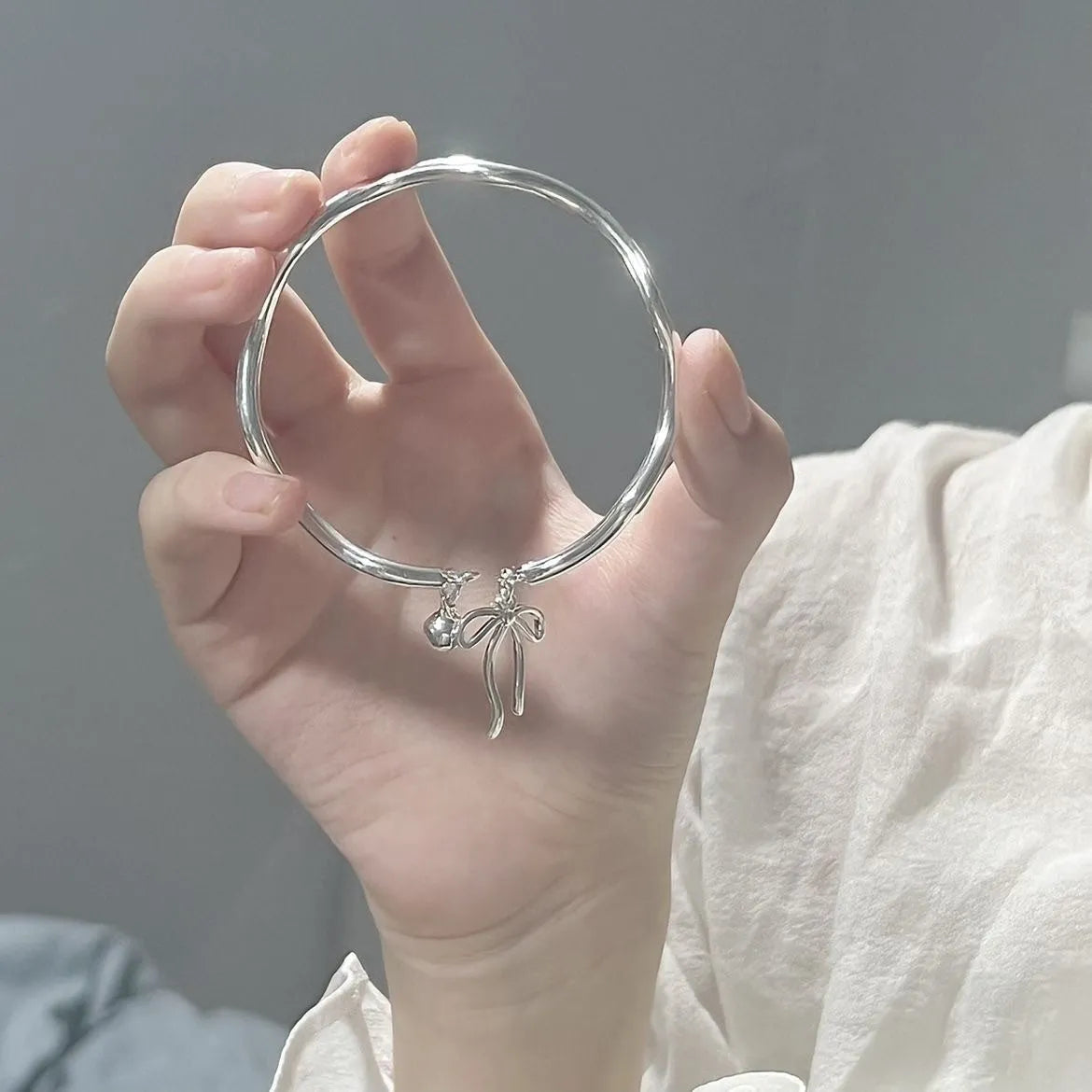 Silver adjustable bracelet with a bow charm and small bell on a zinc alloy band.