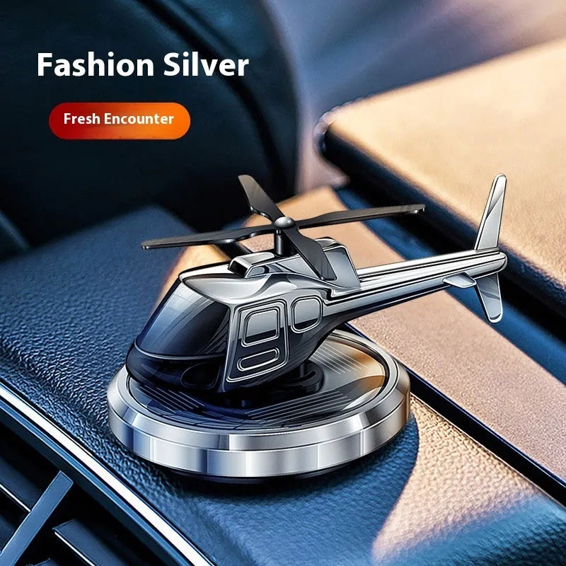 Silver metal solar helicopter car air freshener ornament with rotating blades on dashboard