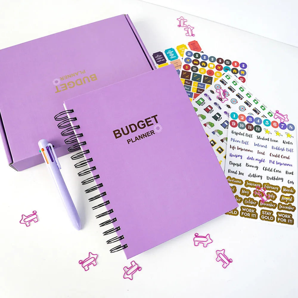 J12 purple coil-bound budget notebook with pen, sticker sheets, and paper clips for financial planning.