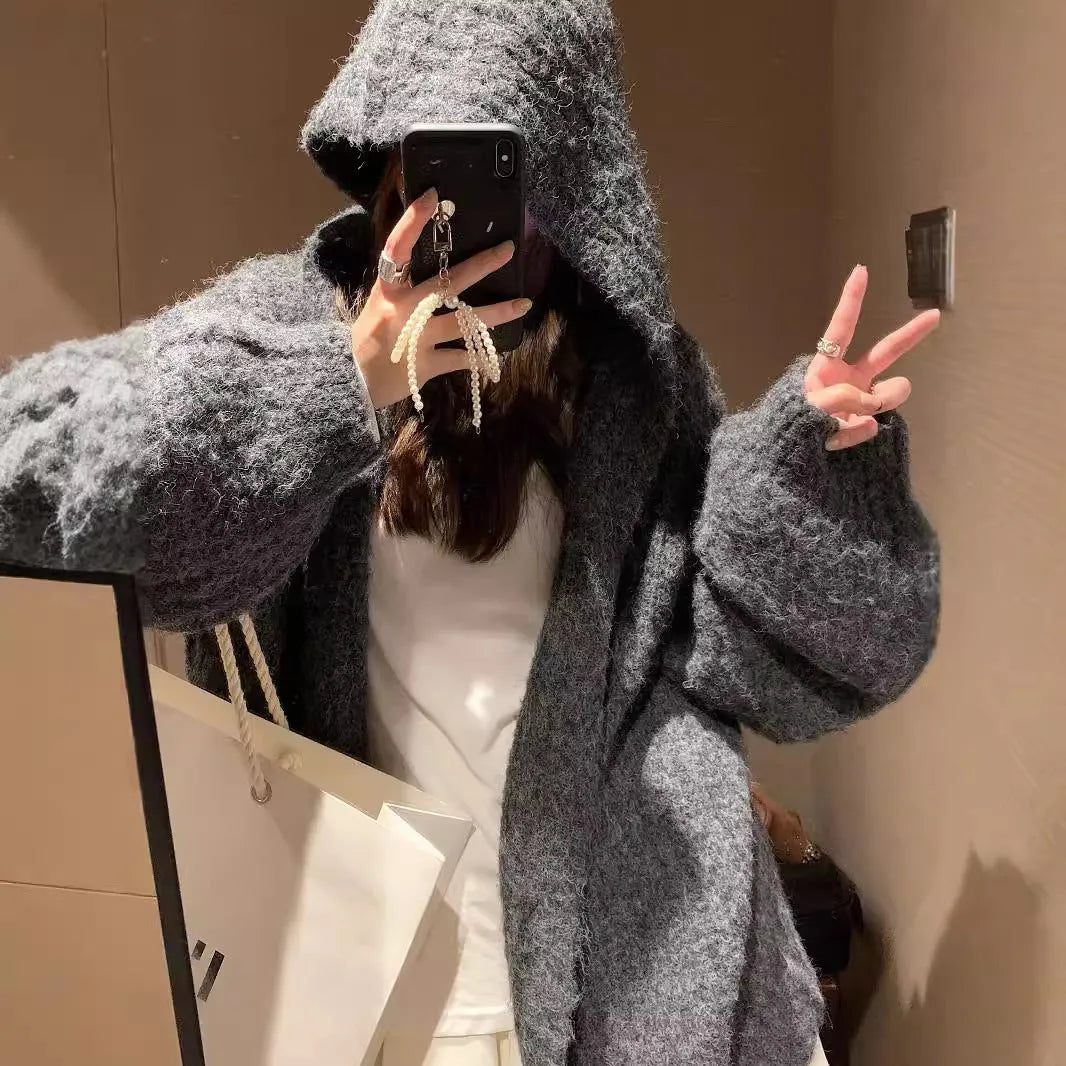 Women's retro-style thick knitted hooded cardigan in dark grey, shown open over a top.