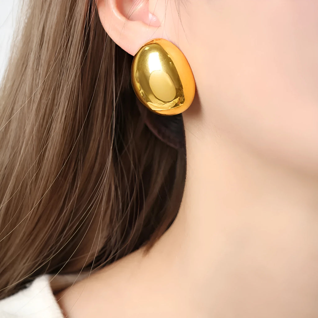 A pair of geometric gold-coloured ear studs with a glazed finish and exaggerated line details on a white background.