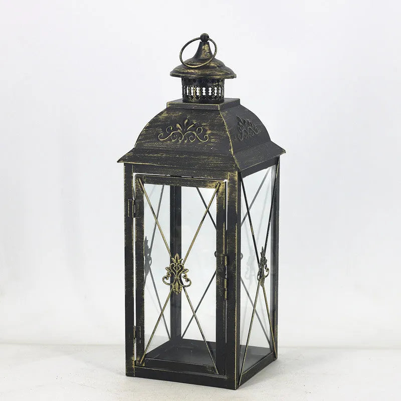 Black and white wrought iron floor-standing storm lantern with clear tempered glass panels on a garden patio.