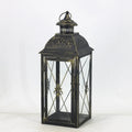 Black and white wrought iron floor-standing storm lantern with clear tempered glass panels on a garden patio.