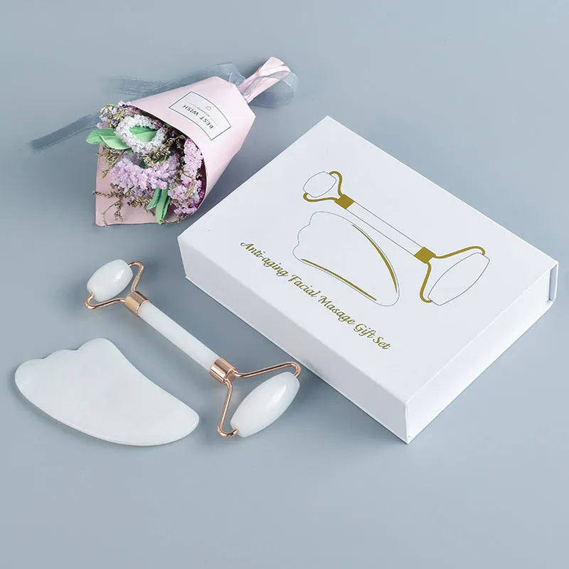 White jade double-headed facial roller and gua sha scraping board set on a plain background.