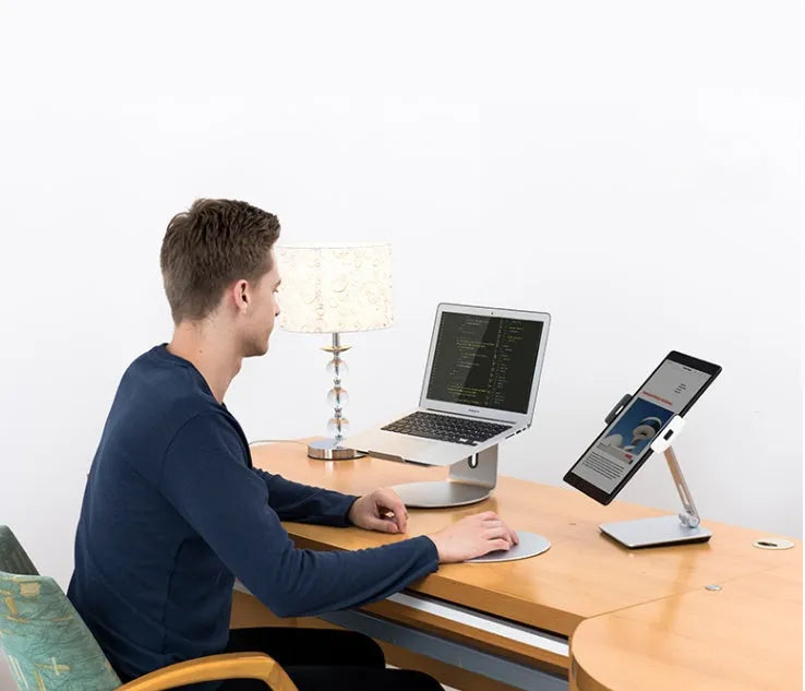 Silver foldable aluminium phone and tablet holder on a desk, showing 360-degree rotation feature.