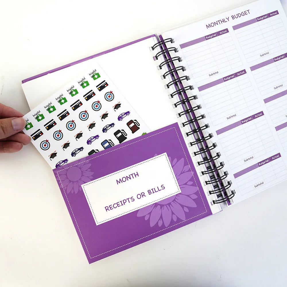 J12 purple coil-bound budget notebook with pen, sticker sheets, and paper clips for financial planning.