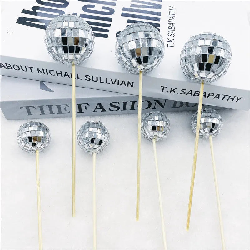 Glass disco ball cake decoration on wooden stick, showing reflective surface.