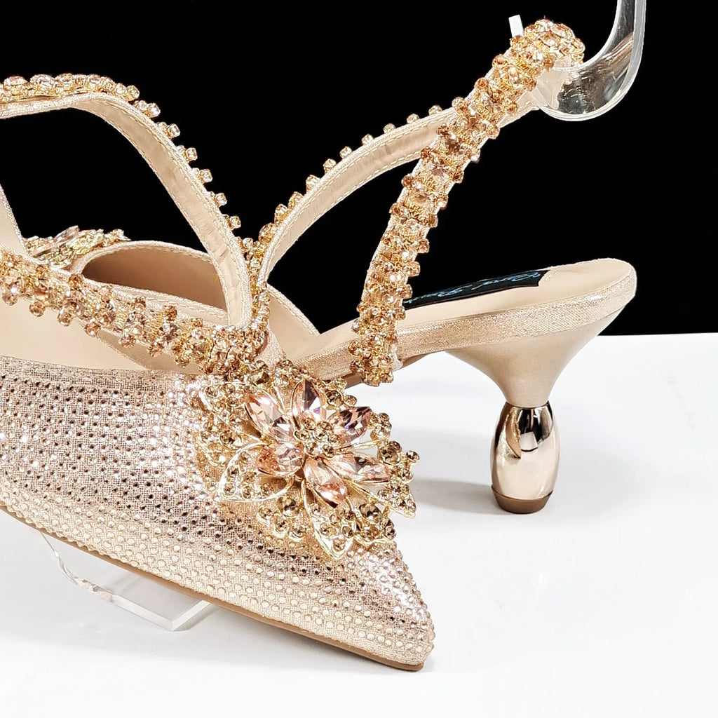Women's black high heel sandal with rhinestone flower decoration and ankle chain, shown with matching clutch bag