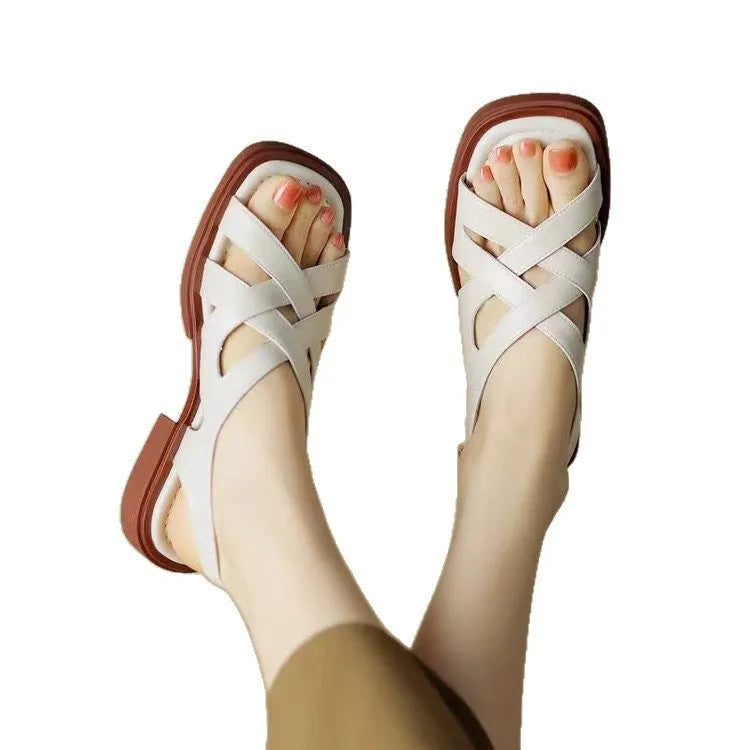 Women's black patent leather square toe beach sandals with cross-band strap on a low rubber sole.