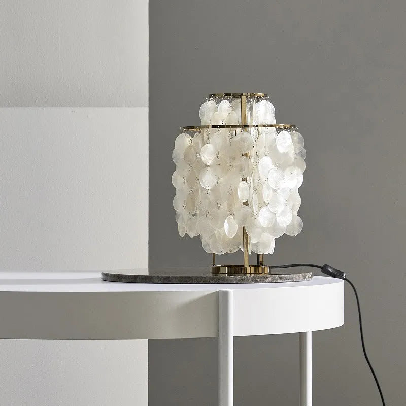 Modern shell-shaped metal bedside table lamp in chrome finish on a wooden table.