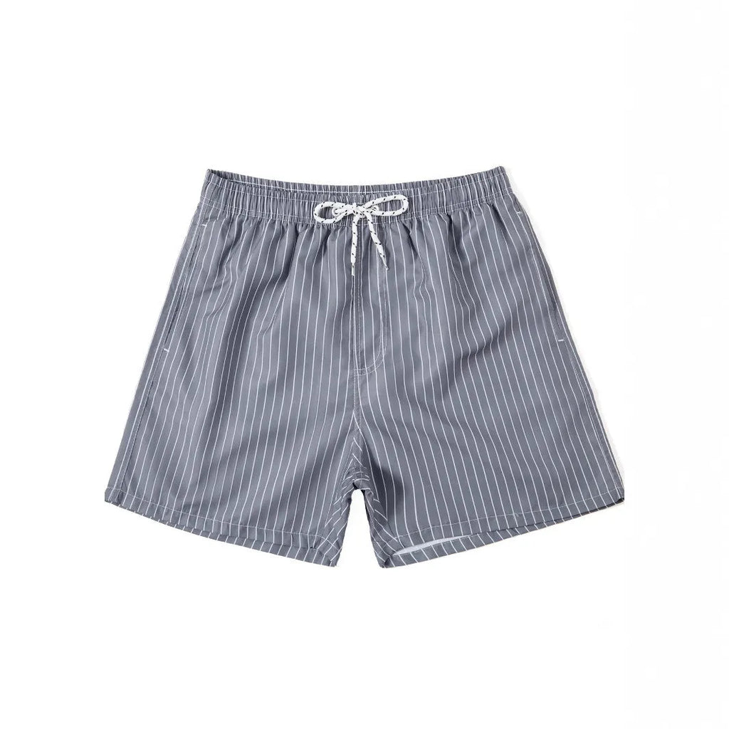 Man wearing grey striped polyester beach shorts with a straight leg opening, on a beach.