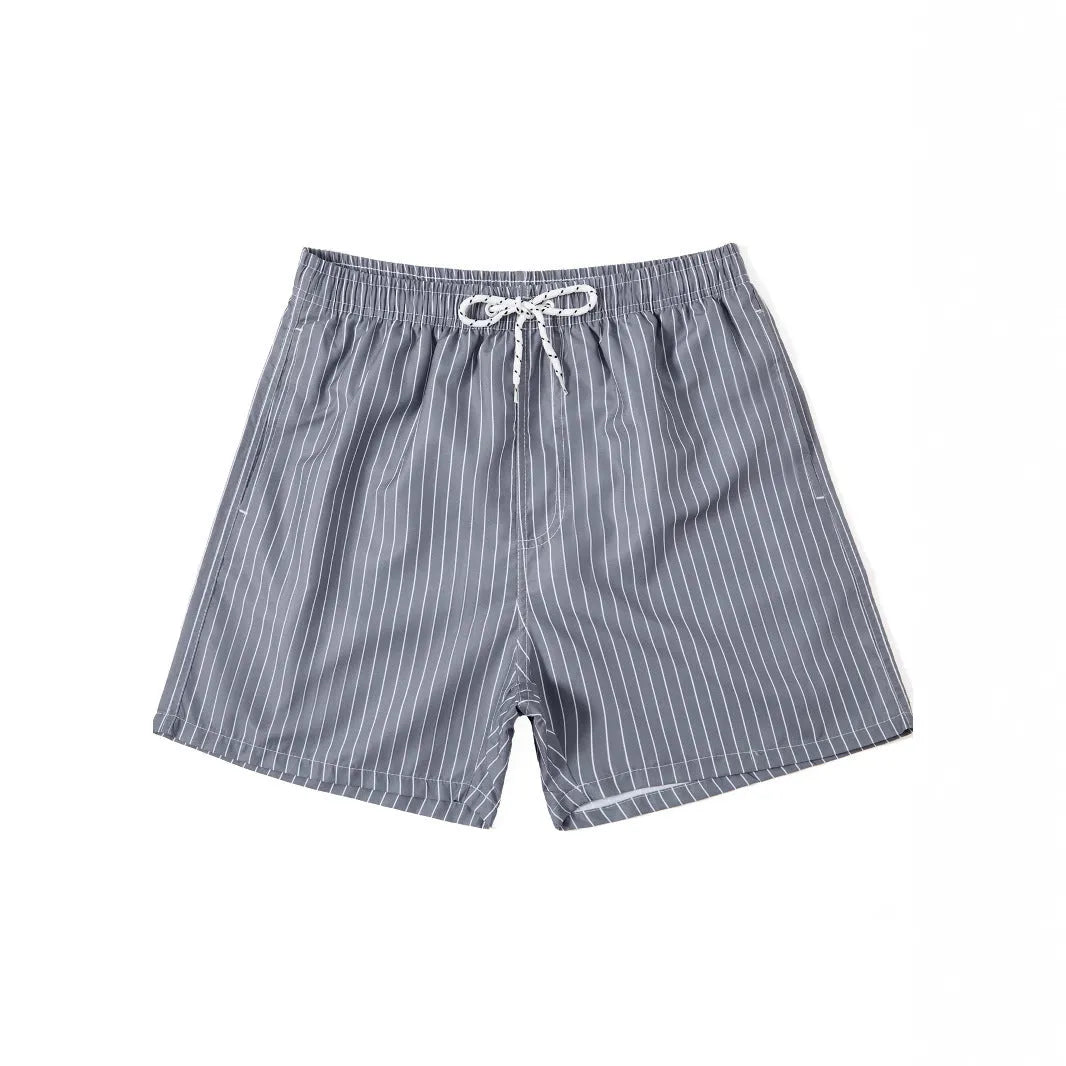 Man wearing grey striped polyester beach shorts with a straight leg opening, on a beach.