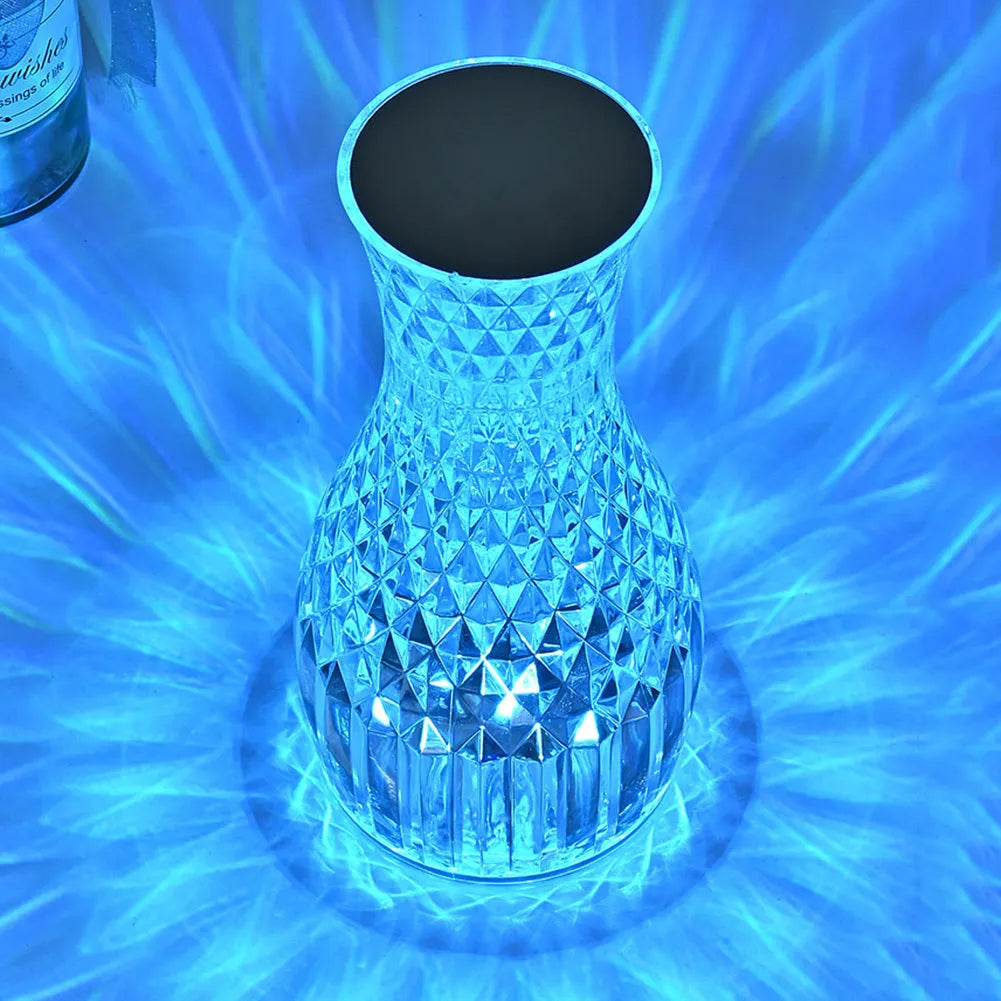 Transparent vase-shaped crystal LED table lamp with multi-colour lights on a wooden table.