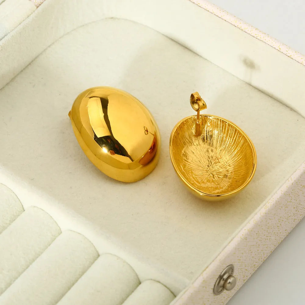 A pair of geometric gold-coloured ear studs with a glazed finish and exaggerated line details on a white background.