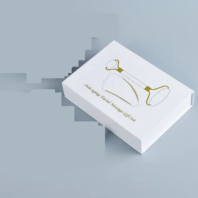 White jade double-headed facial roller and gua sha scraping board set on a plain background.