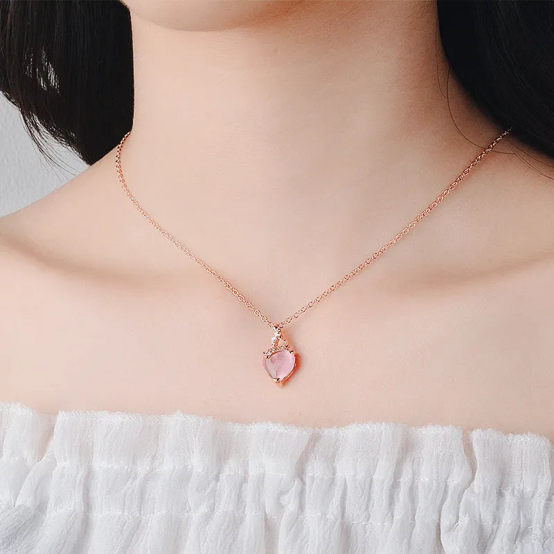 Women's rose gold necklace with a heart-shaped pink crystal pendant on a cross chain.