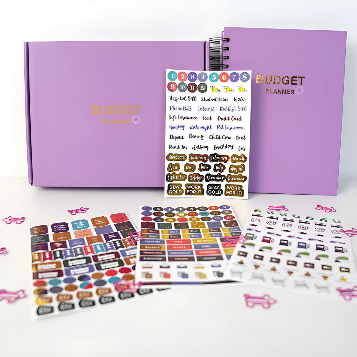 J12 purple coil-bound budget notebook with pen, sticker sheets, and paper clips for financial planning.