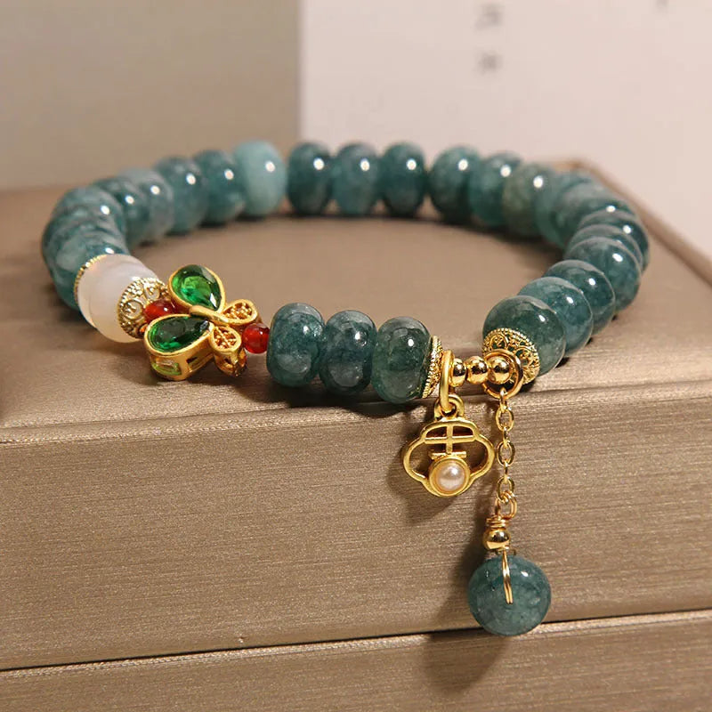 Close-up of a women's bracelet with blue jade and white agate abacus beads, butterfly charms, and rhinestones on an alloy chain.