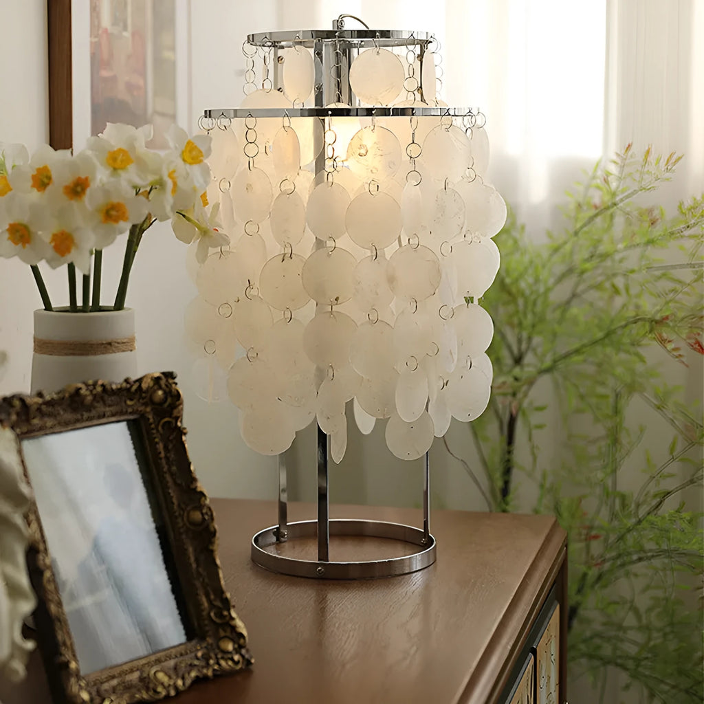 Modern shell-shaped metal bedside table lamp in chrome finish on a wooden table.
