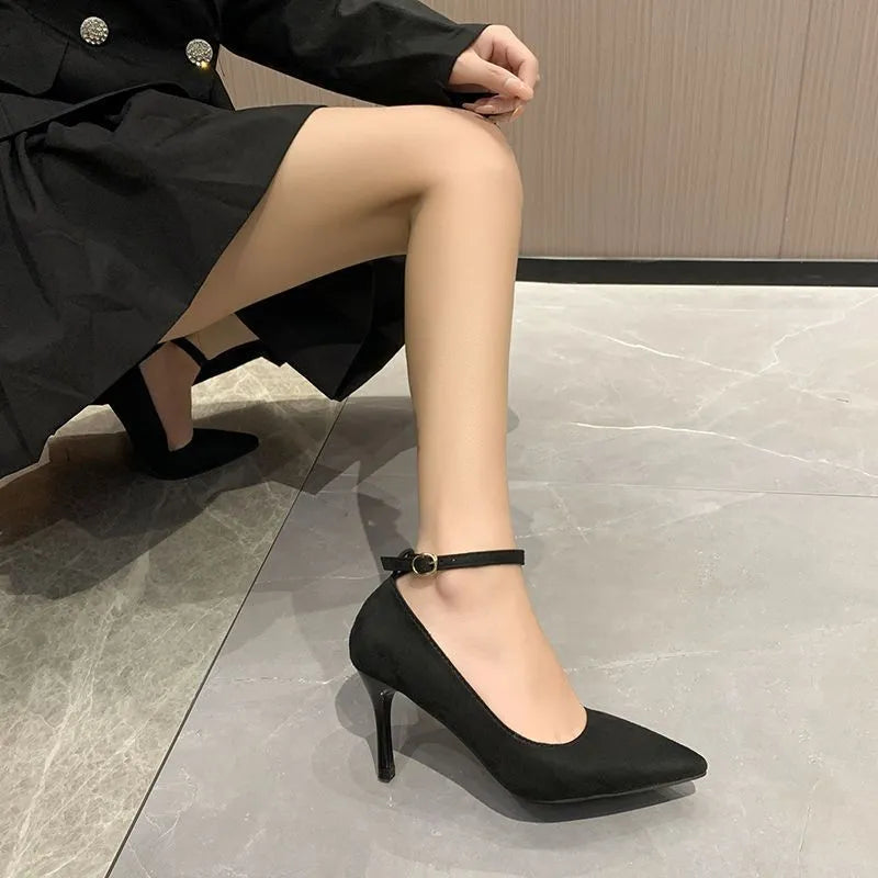 Women's black stiletto pump with buckle closure and skull pattern, shown on a foot.