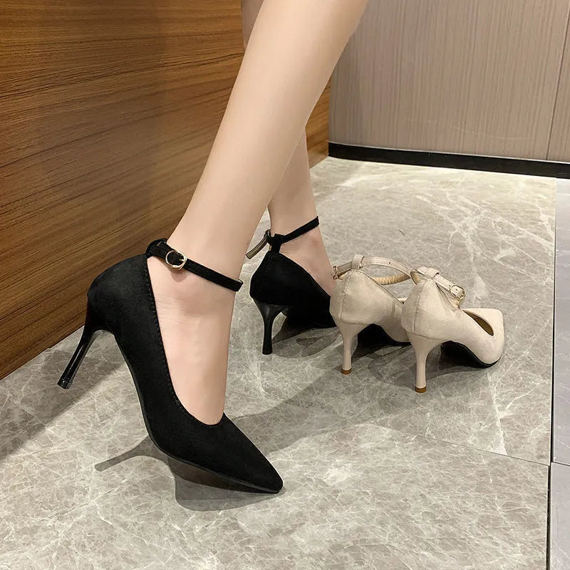 Women's black stiletto pump with buckle closure and skull pattern, shown on a foot.