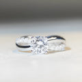 Close-up of a twisted sterling silver band moissanite ring with a four-claw setting and geometric lines.