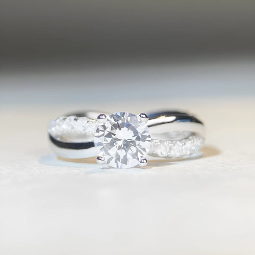 Close-up of a twisted sterling silver band moissanite ring with a four-claw setting and geometric lines.
