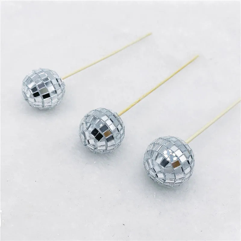 Glass disco ball cake decoration on wooden stick, showing reflective surface.