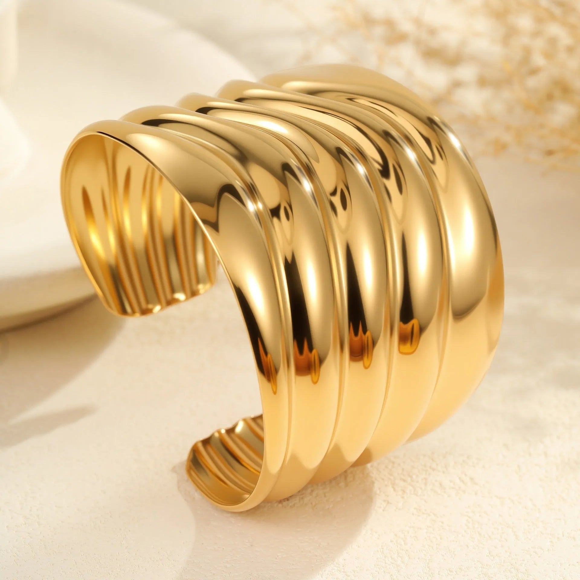 Women's stainless steel bracelet with 18K gold plating featuring geometric wave design and exaggerated wide band