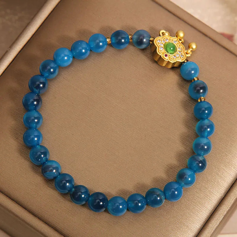 Close-up of a women's bracelet with a blue sugar heart agate safety lock pendant, crystal links, and rhinestone details.