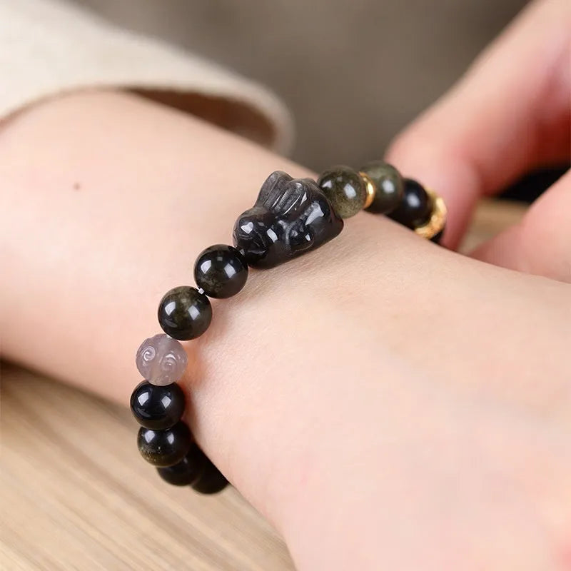 Handmade lying rabbit obsidian bracelet with grey agate beads and brass details on a wrist.
