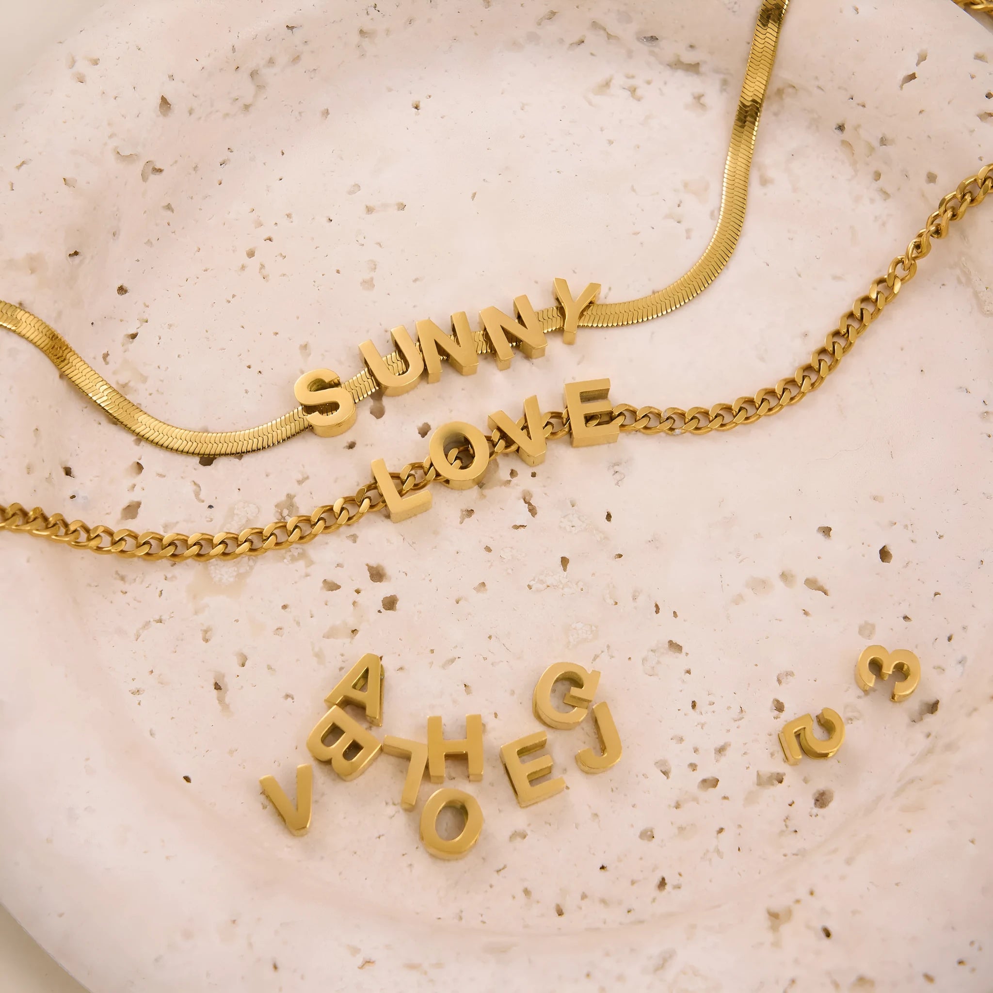 A gold and a silver titanium steel necklace with letter and number pendants on a 40.5cm chain.