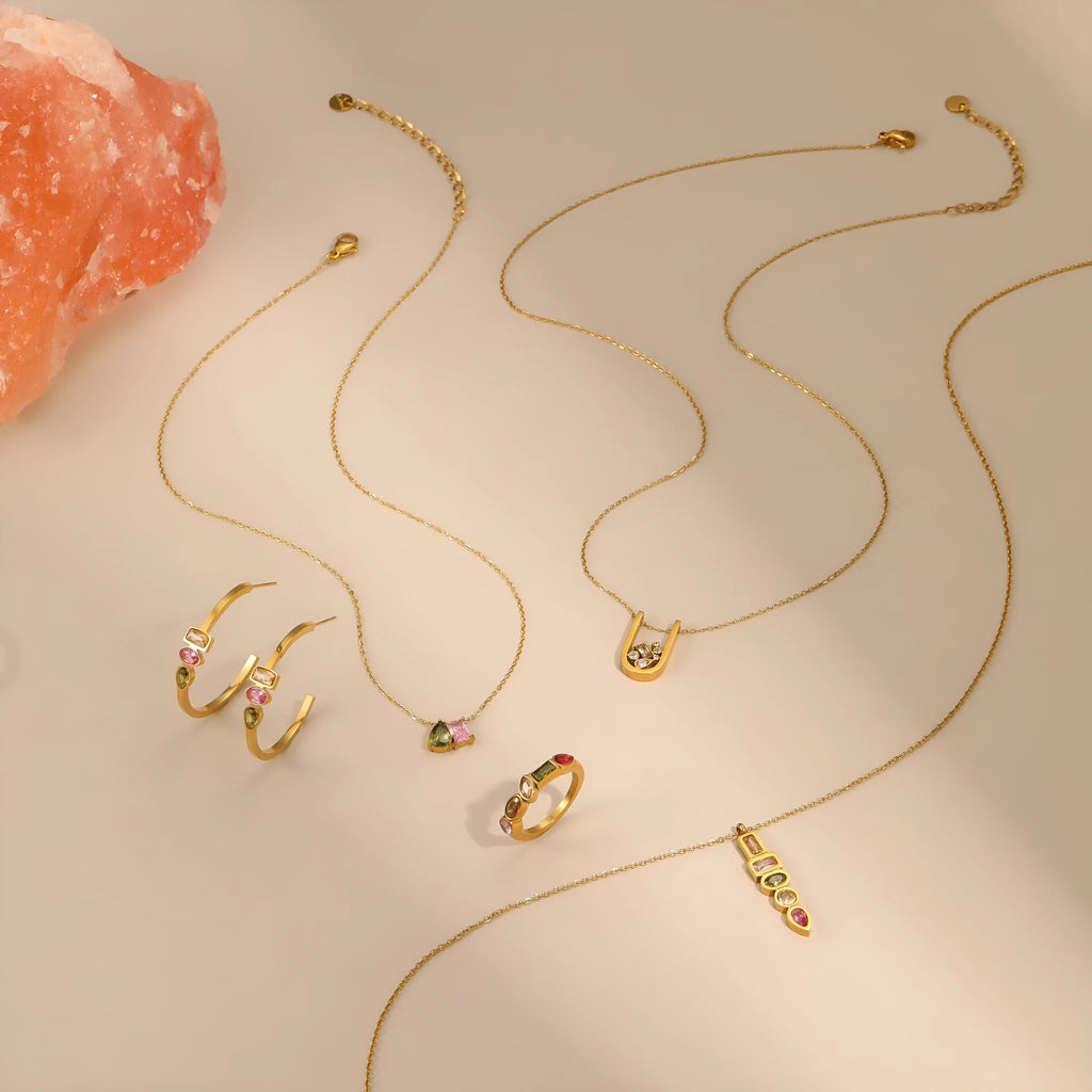 Geometric gold plated jewellery set on display showing drop necklace, U shape necklace, ring, and earrings with zircon accents.
