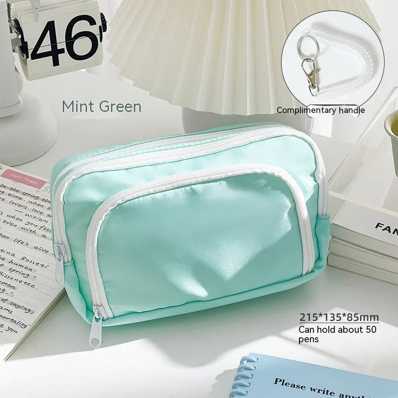 Double layer zippered pencil case in blue with a gift handle, shown next to pens and pencils.