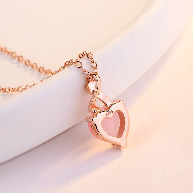 Women's rose gold necklace with a heart-shaped pink crystal pendant on a cross chain.