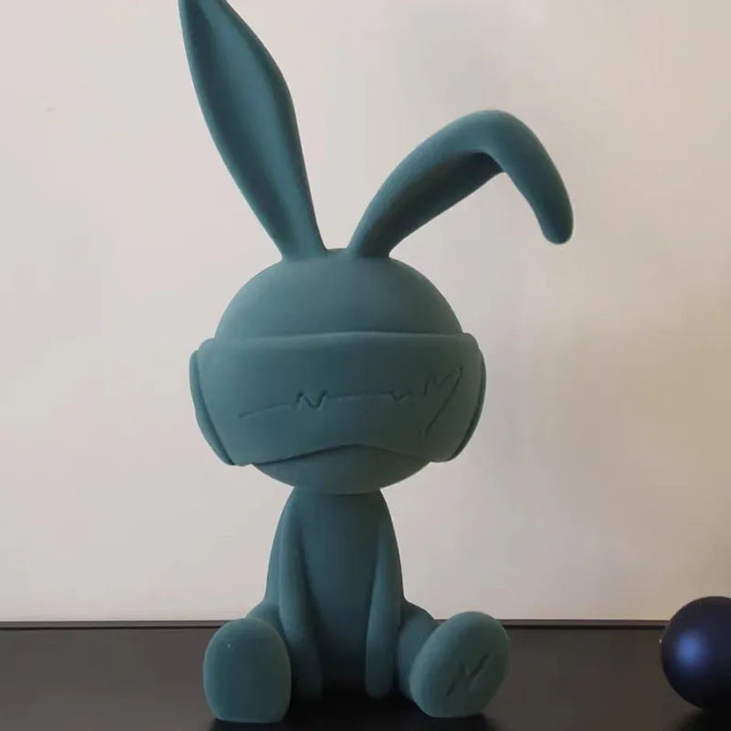 Resin table ornament of a rabbit wearing a suede blindfold with ribbon and tassel detail.