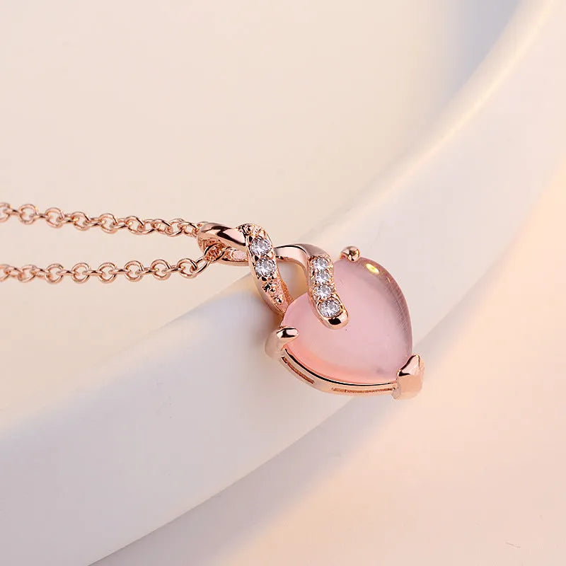 Women's rose gold necklace with a heart-shaped pink crystal pendant on a cross chain.