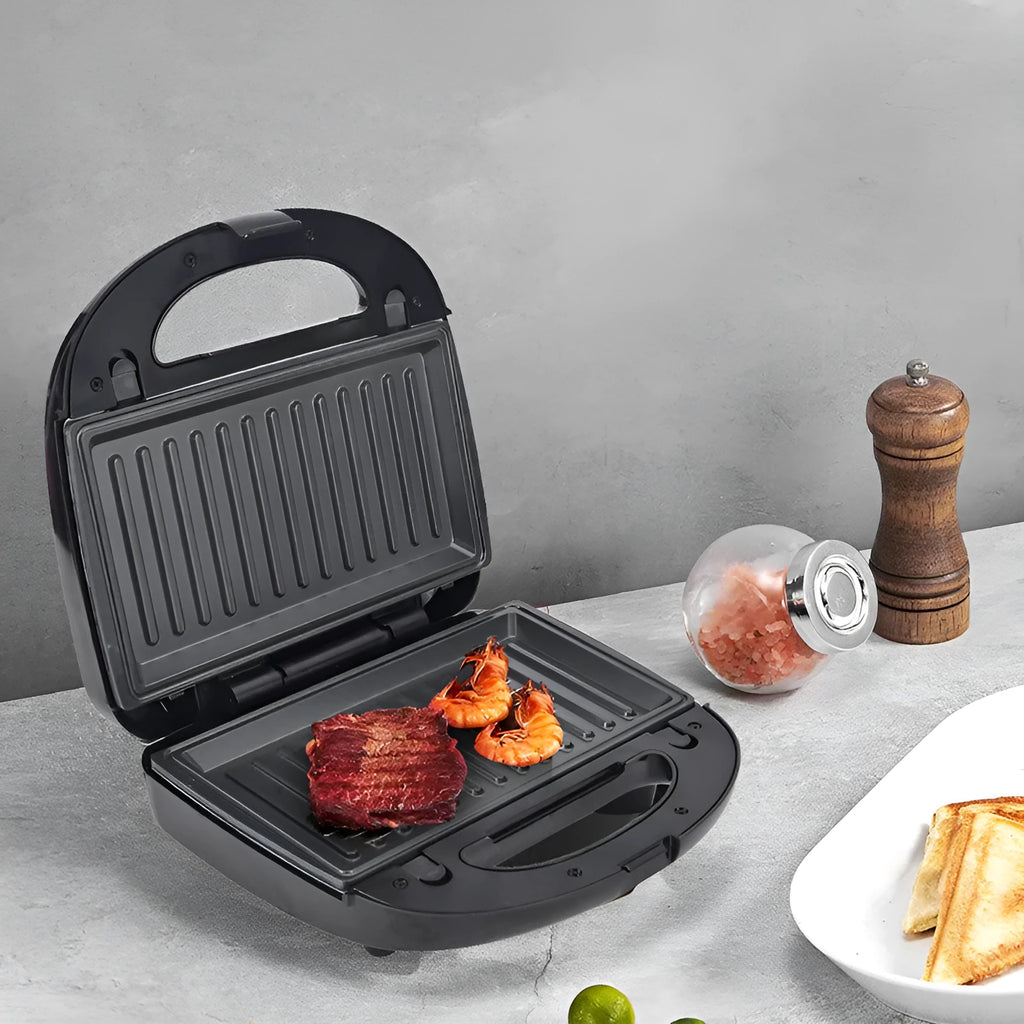 Black electric sandwich pan with stainless steel lid on a kitchen countertop.