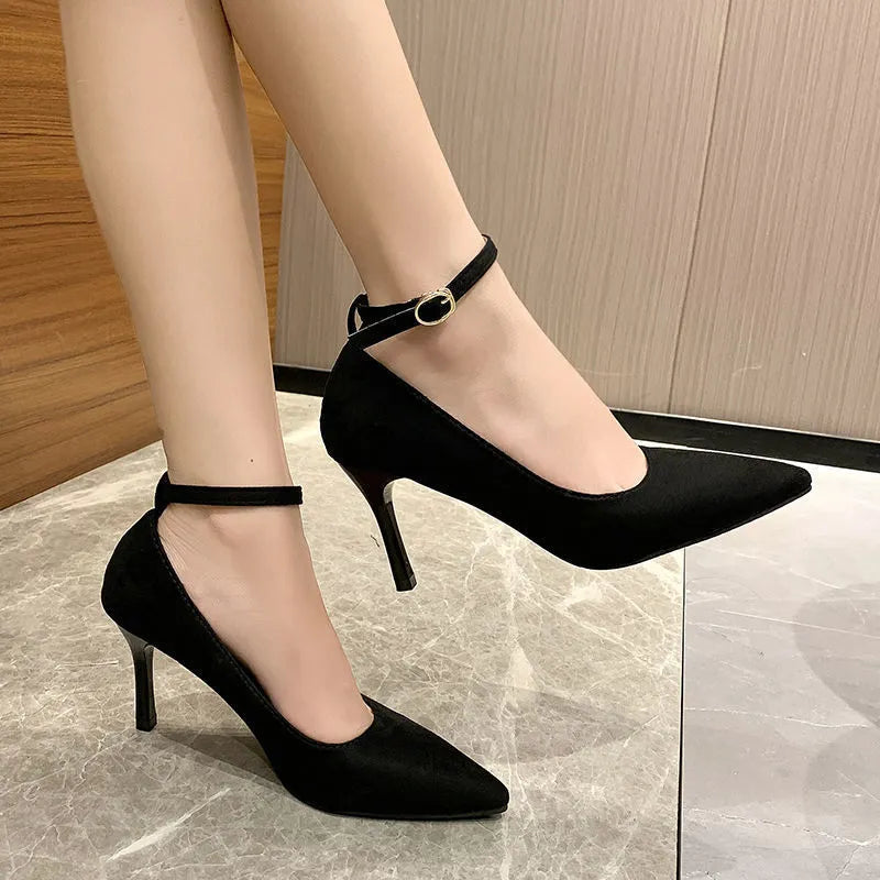 Women's black stiletto pump with buckle closure and skull pattern, shown on a foot.