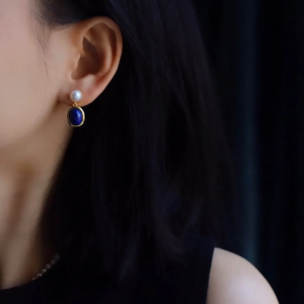 A pair of simple sterling silver earrings featuring blue lapis lazuli pearls and auspicious pattern detailing.