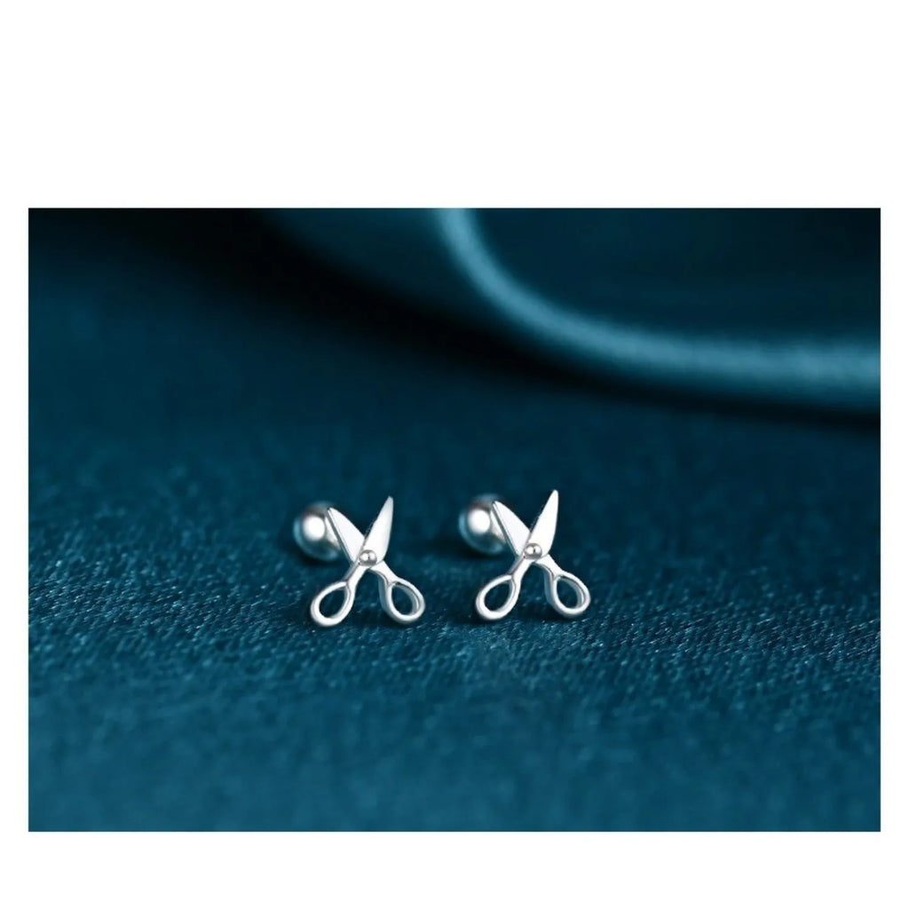 A pair of silver screw-back ear nails with a miniature scissors design on the screw component.