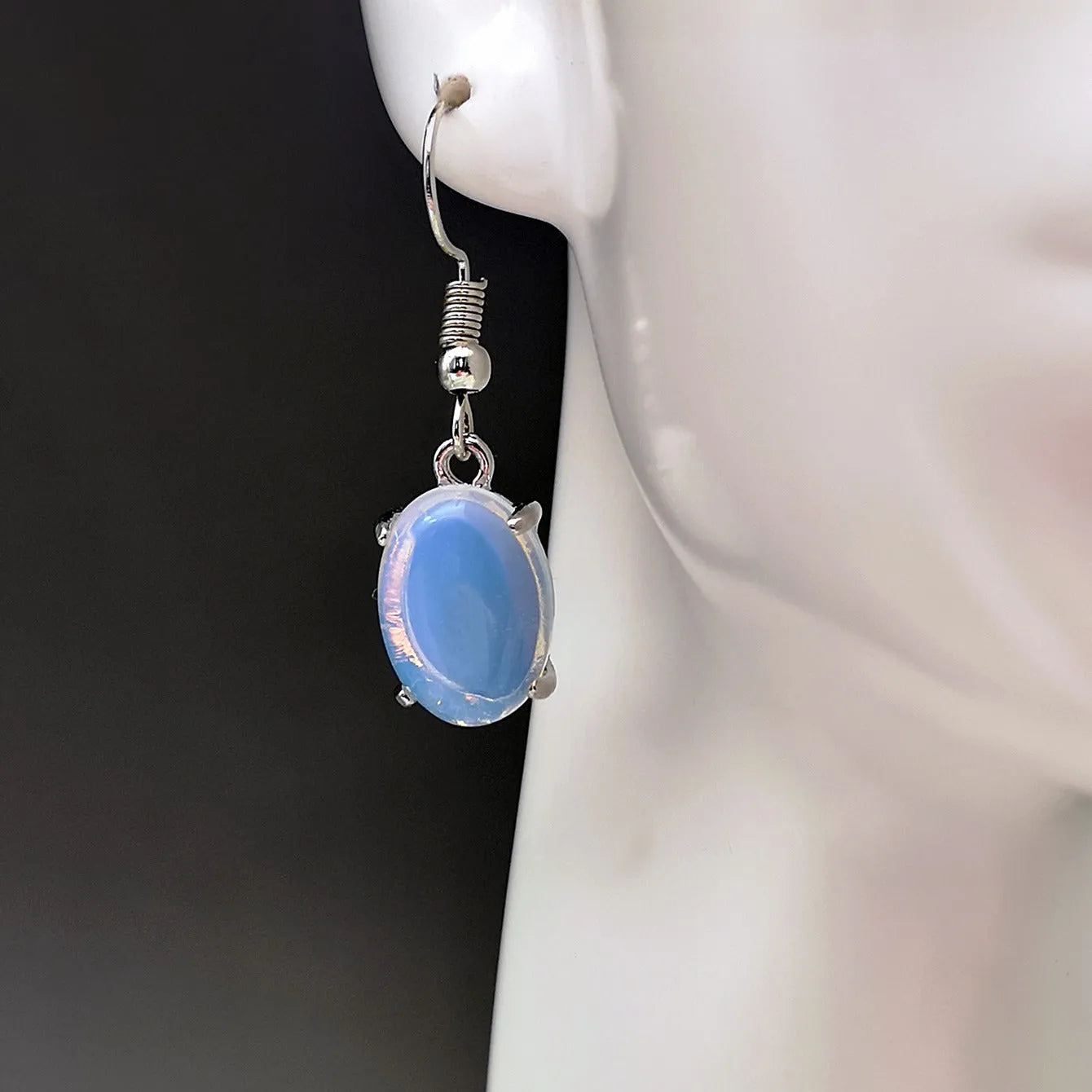 A pair of retro-style opal drop earrings in moonlight white with a cross detail and ellipse shapes.