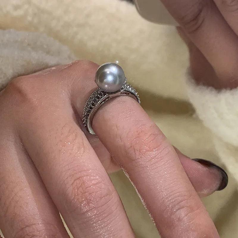 Geometric adjustable open ring in black pearl colour on a copper band, shown on a woman's index finger.