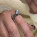 Geometric adjustable open ring in black pearl colour on a copper band, shown on a woman's index finger.