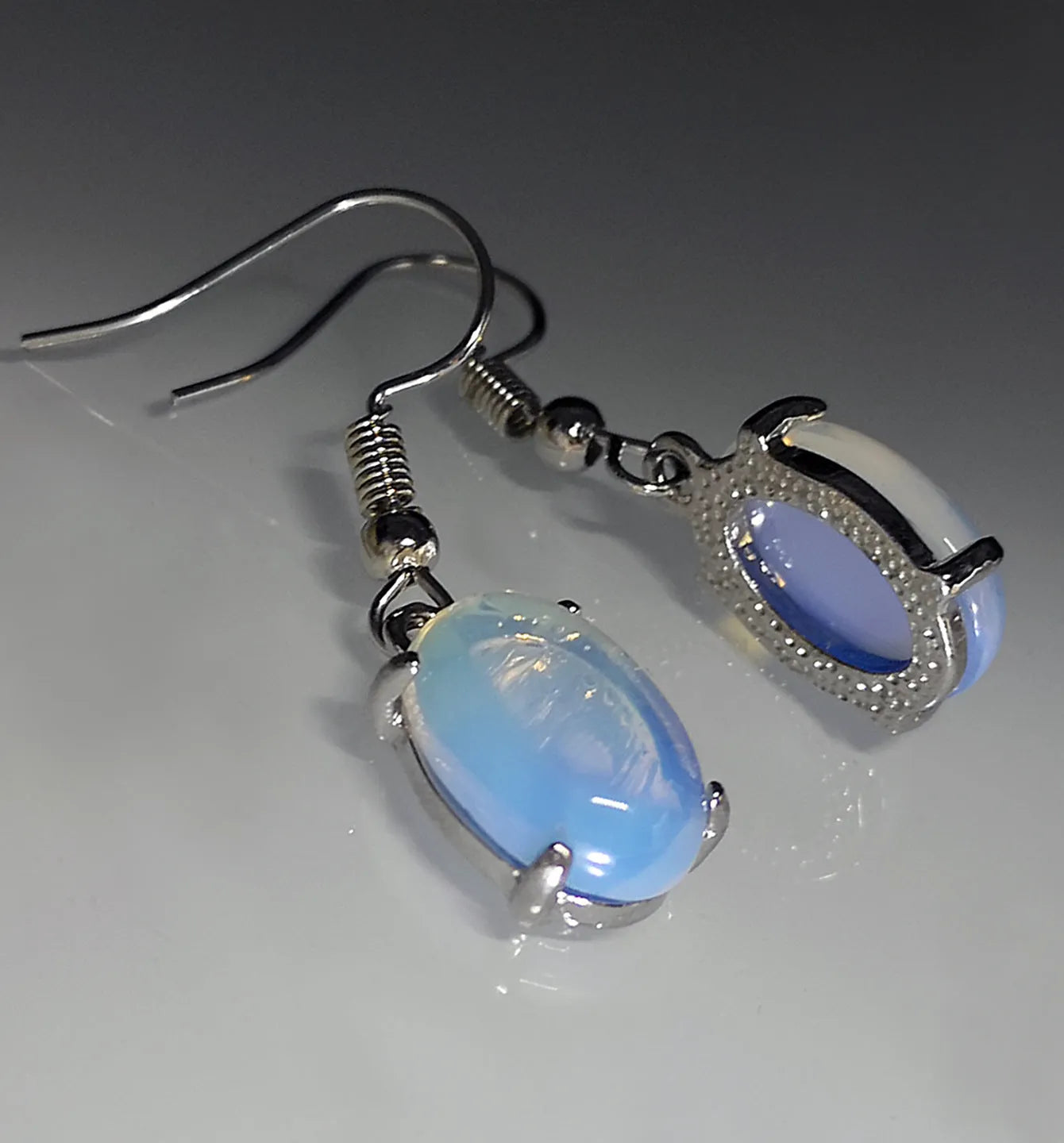 A pair of retro-style opal drop earrings in moonlight white with a cross detail and ellipse shapes.