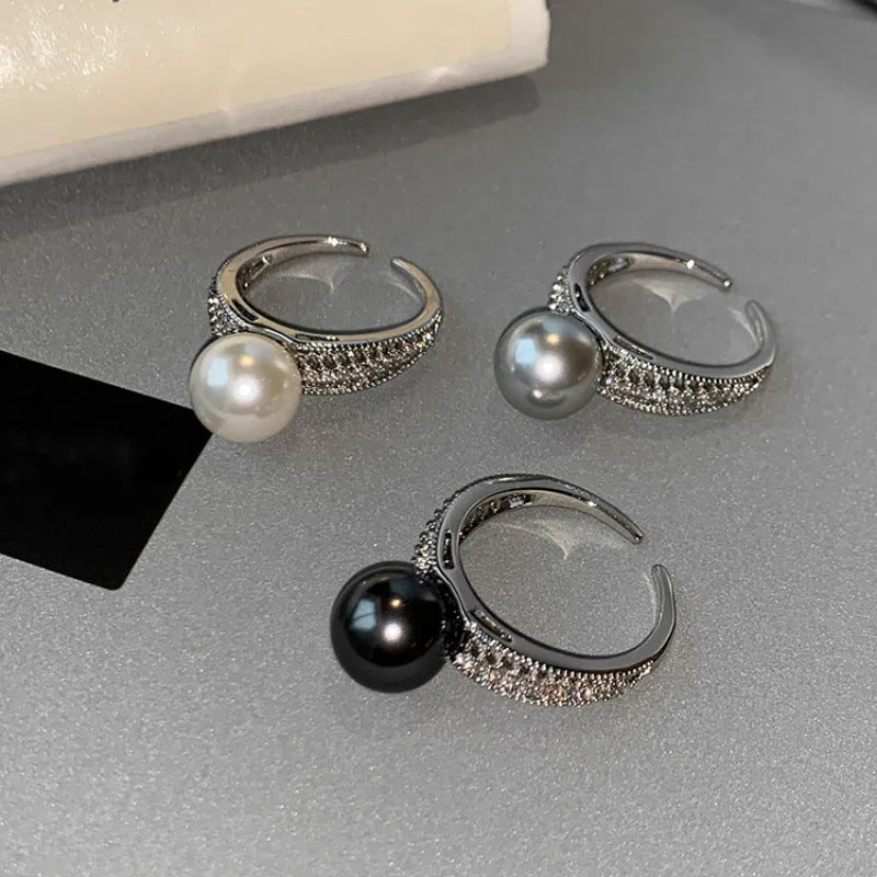 Geometric adjustable open ring in black pearl colour on a copper band, shown on a woman's index finger.