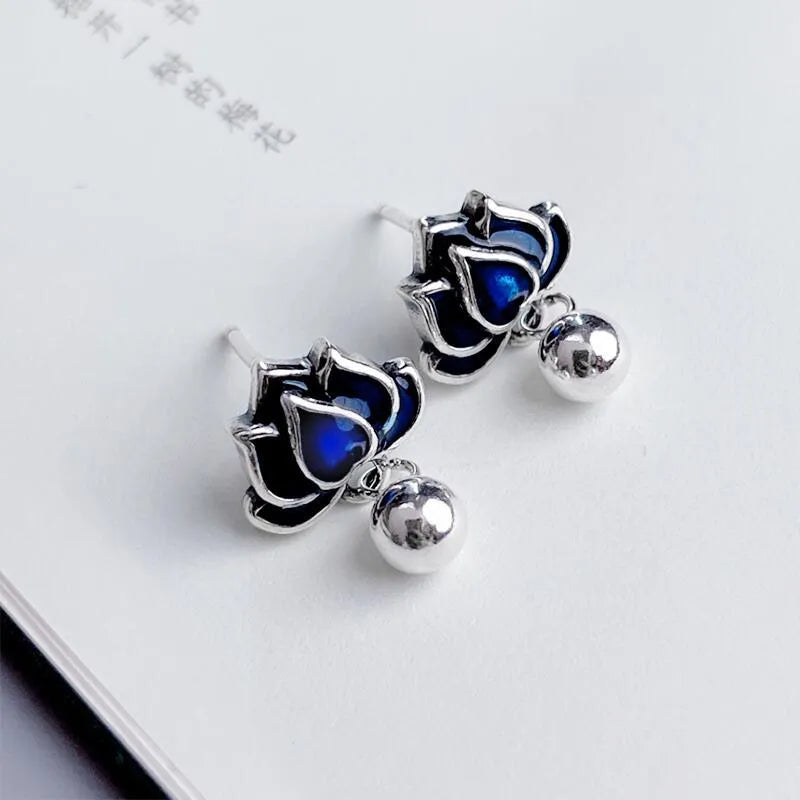 Close-up of blue lotus seedpod and tassel drop earrings in silver tone alloy on a white background.