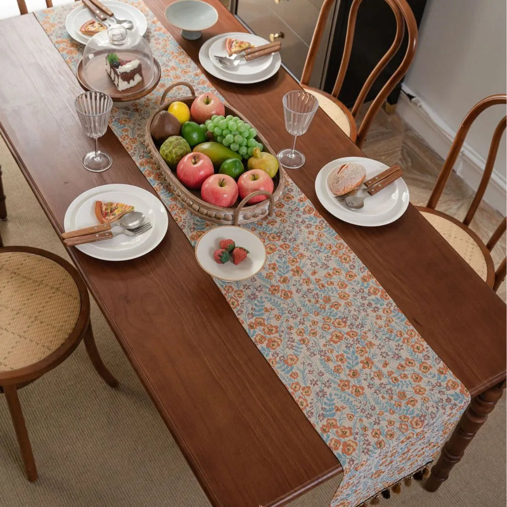 Long beige table runner with floral Jacquard pattern and tassels, shown on a wooden table.
