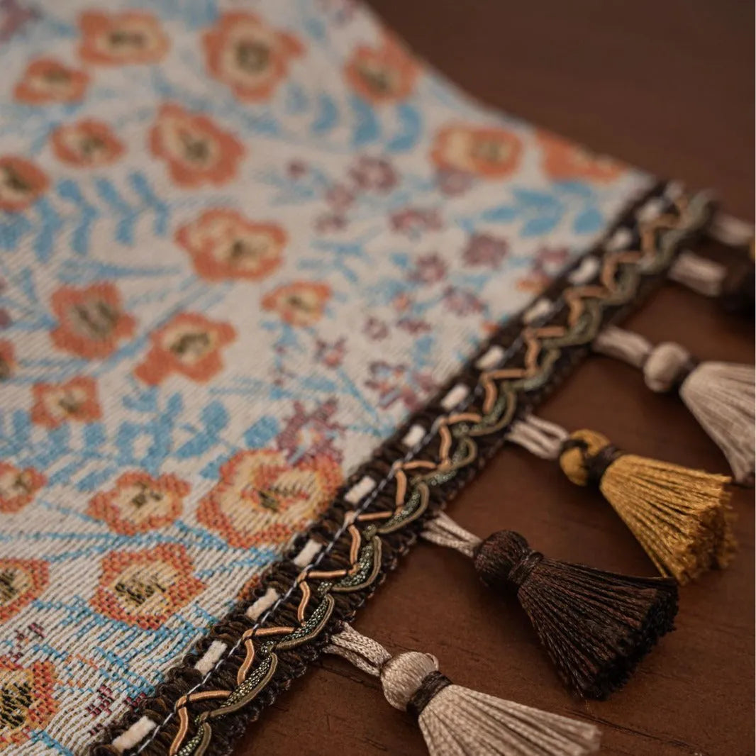 Long beige table runner with floral Jacquard pattern and tassels, shown on a wooden table.